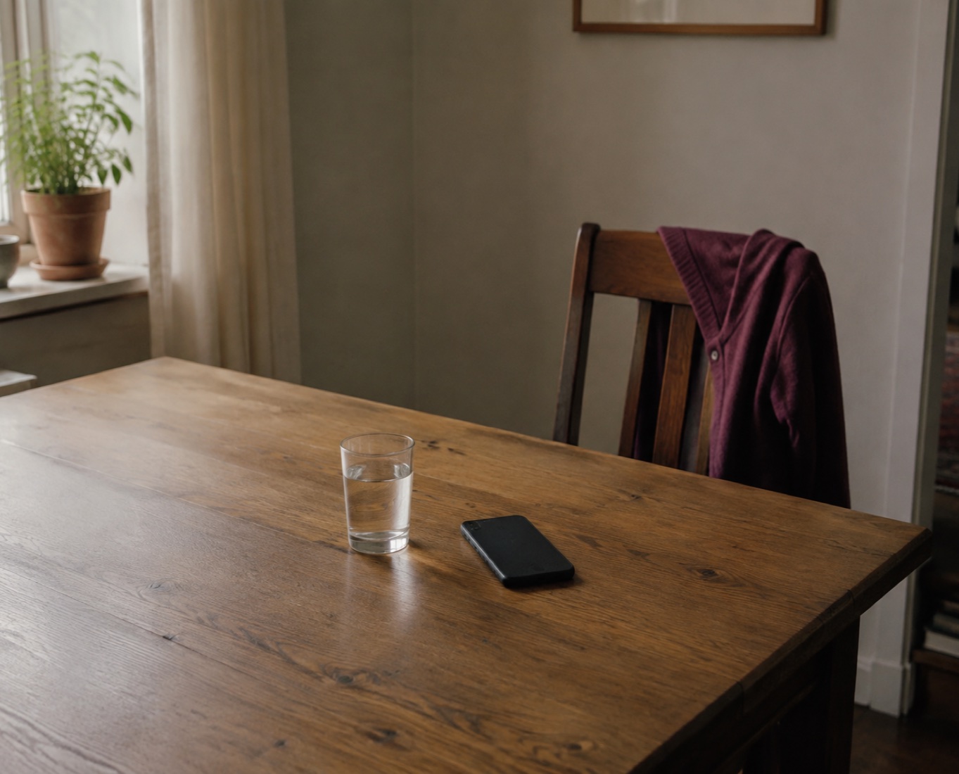 A phone face down beside a glass of water and an empty chair with a plum cardigan.