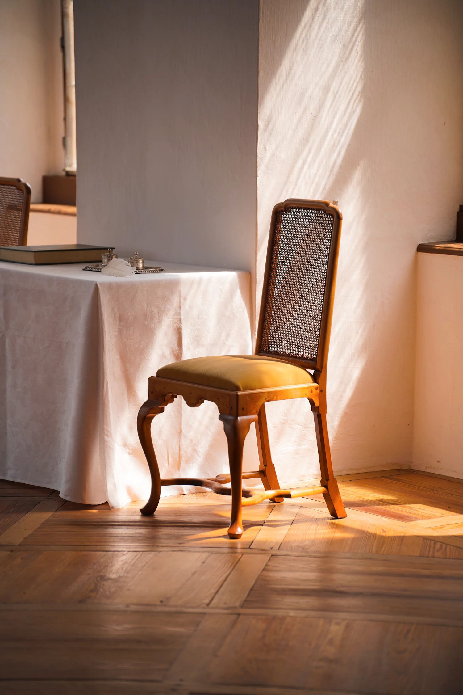 A wooden chair beside a linen-covered table in the morning light.