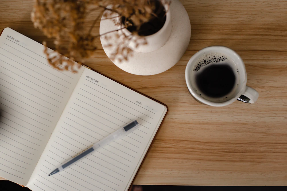 An open notebook and a cup of coffee on a wooden table.