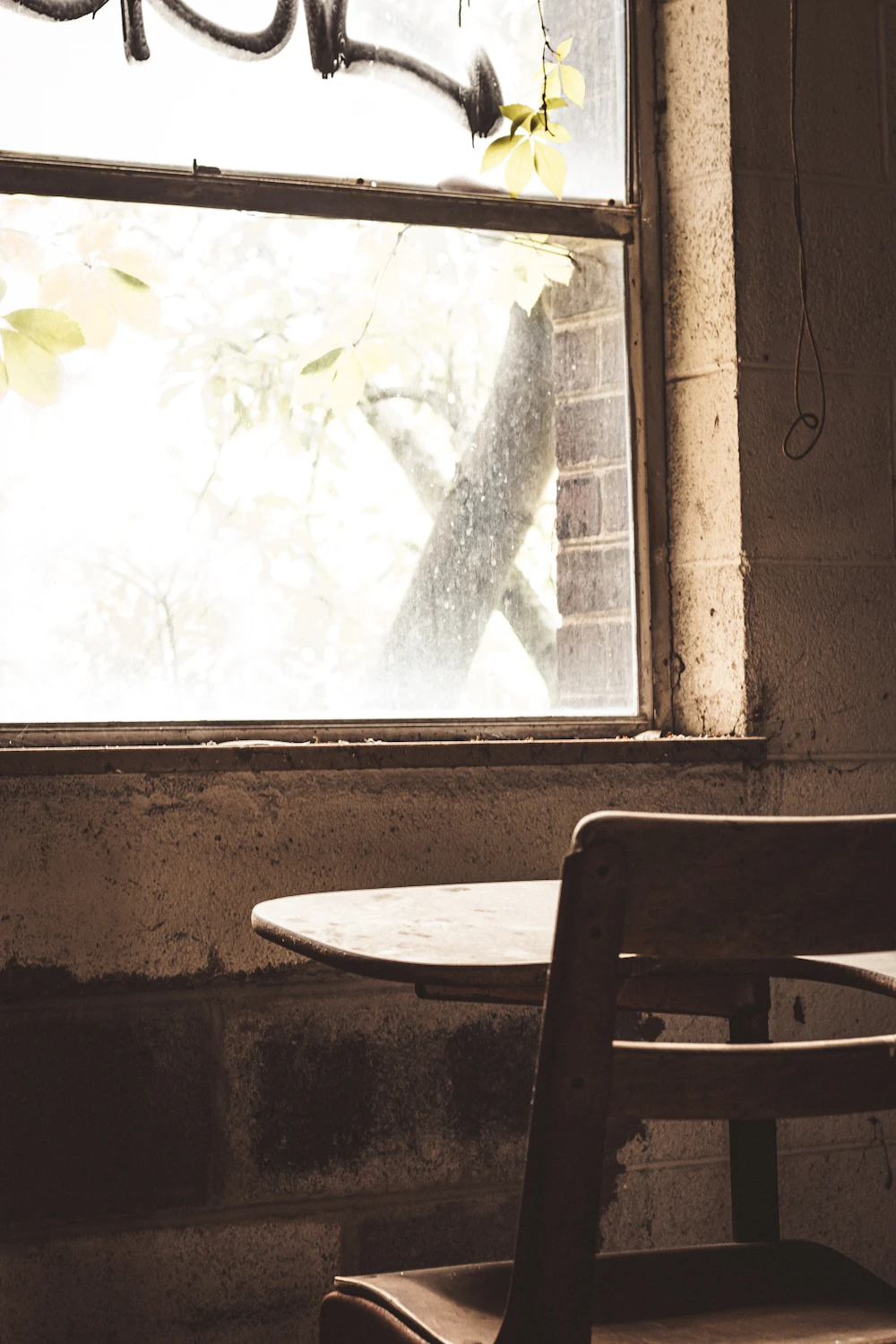 An empty wooden chair and desk beside a sunlit window.